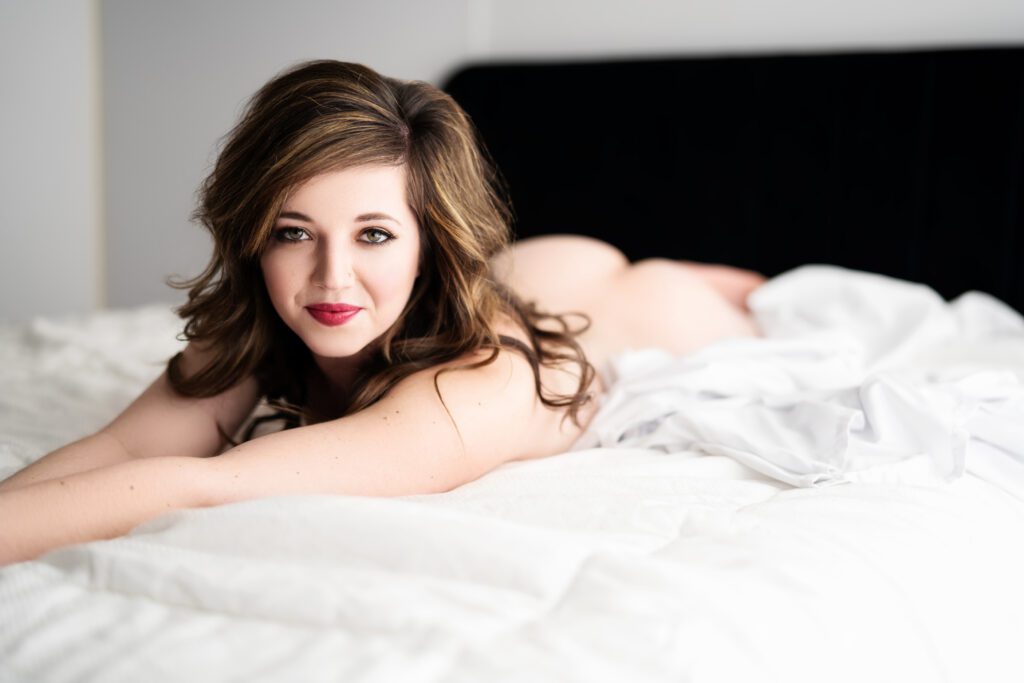 woman laying on white bed with no clothes looking at camera for boudoir photos